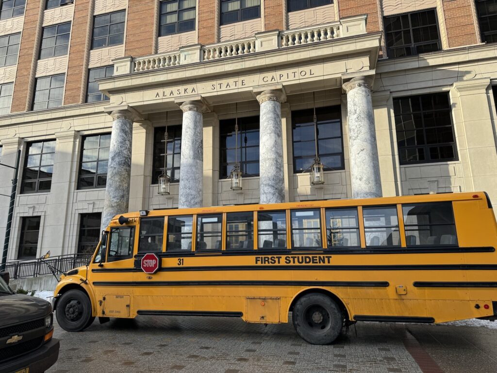 A school bus passes in front of the Alaska Capitol on Tuesday, Feb. 6, 2024. (Photo by James Brooks/Alaska Beacon)